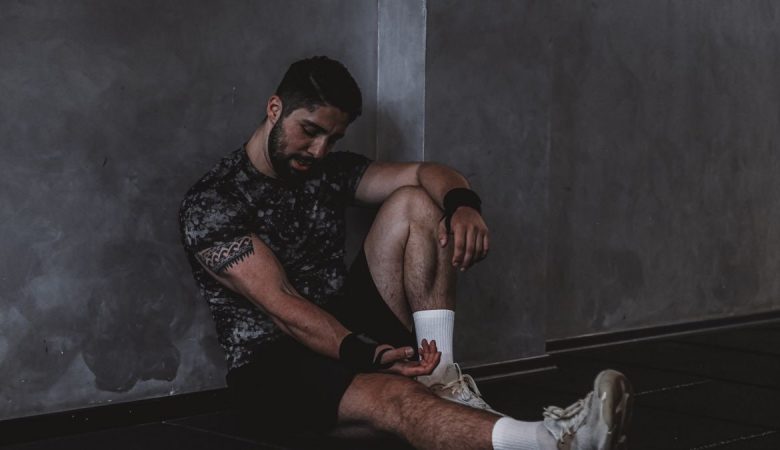 A muscular man in a gym environment taking a moment of rest, reflecting in a dark moody setting.